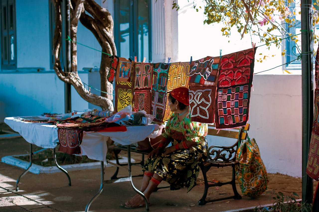 A vibrant street market stall displaying traditional textiles with a seated vendor.
